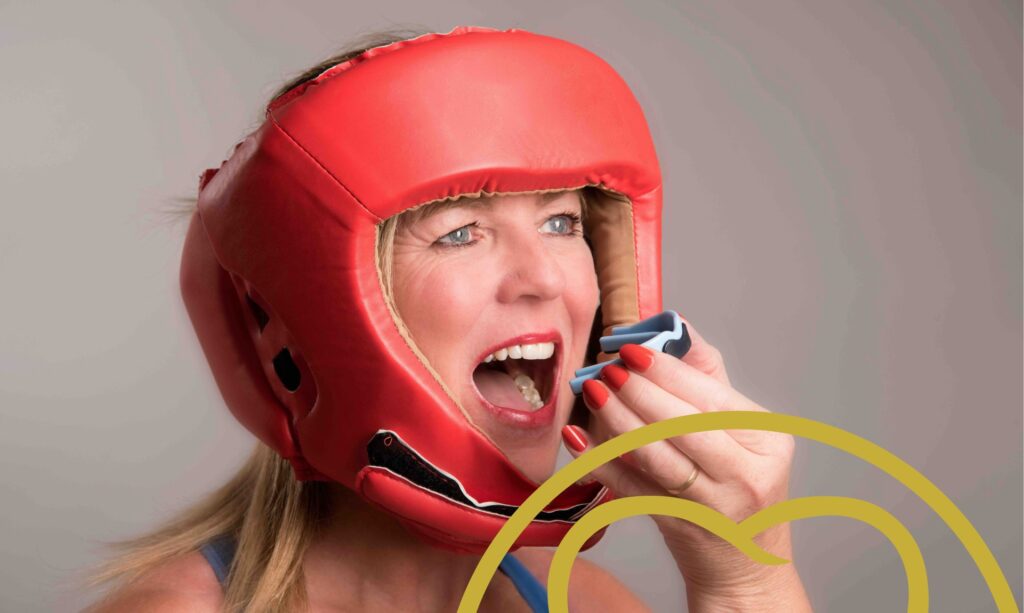 Woman in boxing headgear putting a mouthguard in her mouth